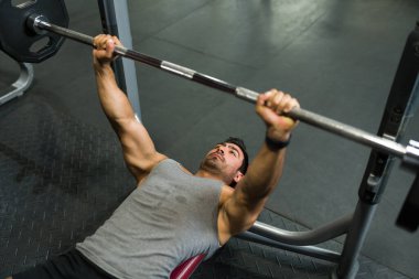 Spor salonunda ağırlık kaldıran ve kaslı bir vücut geliştiren terli bir gencin yüksek açısı.
