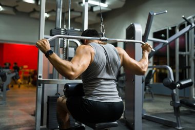 Arkadan spor makinesiyle ağırlık egzersizi yaparken görülen sağlıklı genç adam.