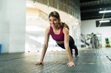 Spor salonunda şınav çekerken gülümseyen mutlu kadın. Atletik kadın spor yapıyor ve neşeli hissediyor.