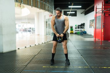 Spor salonunda ağırlık çalışırken kettlebell kullanan kaslı, yakışıklı genç bir adam.