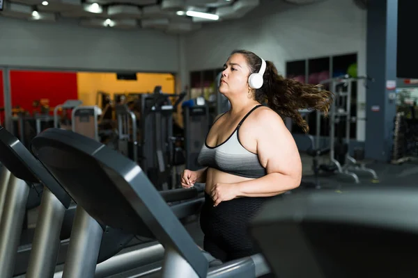 Active obese woman trying a  healthy lifestyle and running on the treadmill at the gym while listening to music with headphones