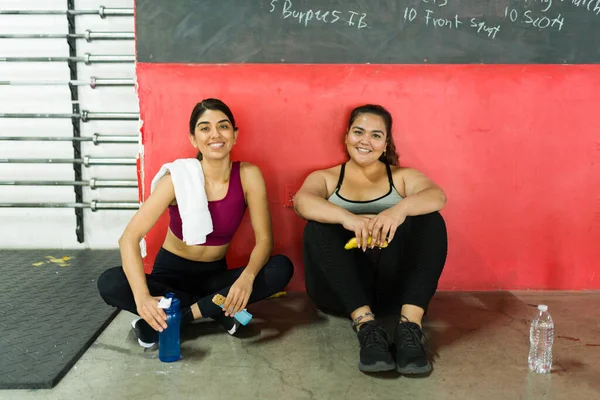 Portrait of a happy fitness coach and an overweight young woman smiling while resting before a workout routine at the gym
