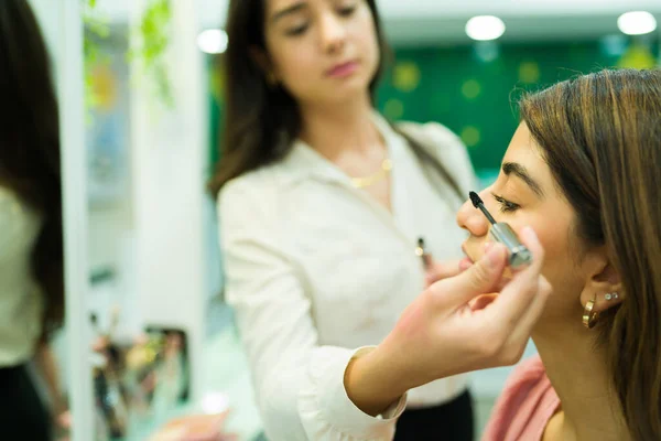在化妆品店 一位化妆师在一位年轻貌美的女士身上涂睫毛膏 — 图库照片