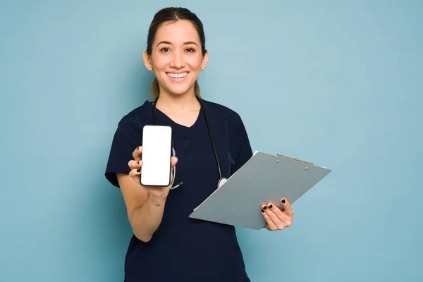 若い女性医師がスマートフォンの画面にモバイルアプリを表示し スタジオで笑顔 — ストック写真
