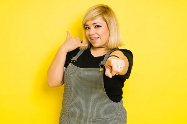 Big Caucasian woman in casual clothes making a gesture of giving her a call against a yellow background