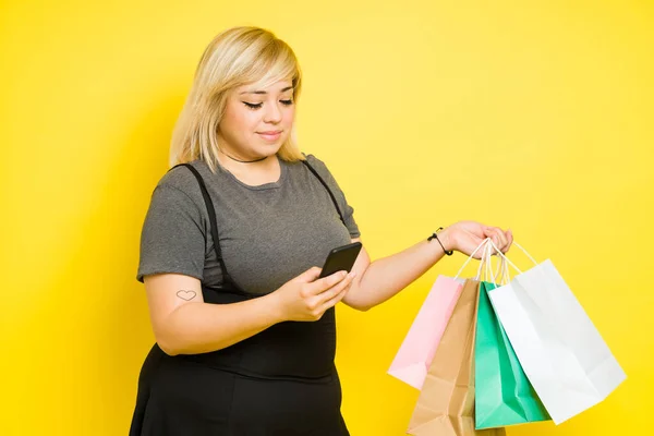 たくさんの買い物袋を持っている間 オンラインで買い物をするために彼女のスマートフォンを使用して髪を染めた大きな女性 — ストック写真
