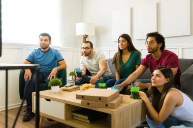 20 'li yaşlarda spor hayranları oturma odasındaki kanepede otururken Amerikan futbolunu izliyorlar. 