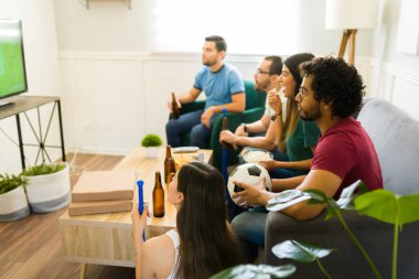 Latin genç arkadaşlar ve spor hayranları birlikte takılırken televizyonda futbol izliyorlar.