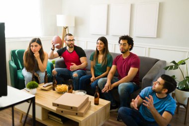 Oturma odasında birlikte maç izlerken futbol oynayan bir grup arkadaş.