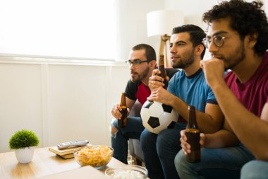 Gergin spor hayranları kanepede oturup, konsantre olup, bira eşliğinde futbol maçı izliyorlar.