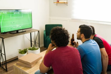 Arkadan bir grup arkadaş oturma odasında bira içerken futbol maçı izlerken görülmüşler.