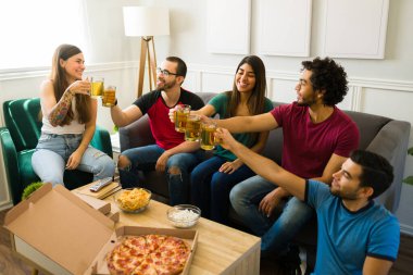 Mutlu genç erkekler ve kadınlar birayla kadeh kaldırırken ve evde pizza ve atıştırmalık yerken mutlu hissederken