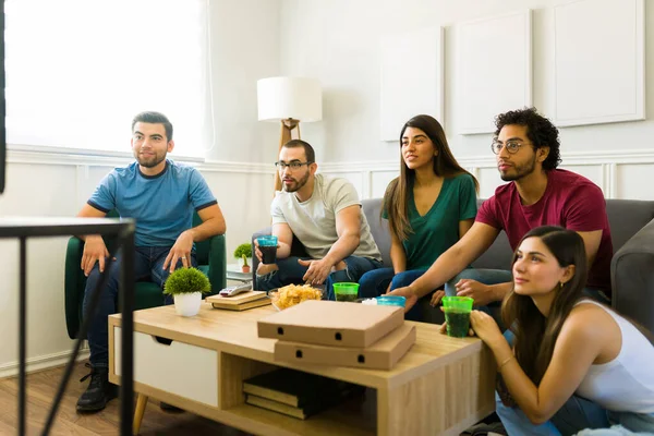 20 'li yaşlarda spor hayranları oturma odasındaki kanepede otururken Amerikan futbolunu izliyorlar. 