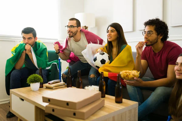 Tv izlerken ulusal futbol takımlarını desteklemek için ülke bayrakları olan endişeli kadınlar ve erkekler
