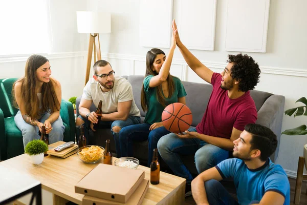 Cheerful friends making a high five and feeling excited while watching a basketball game on tv