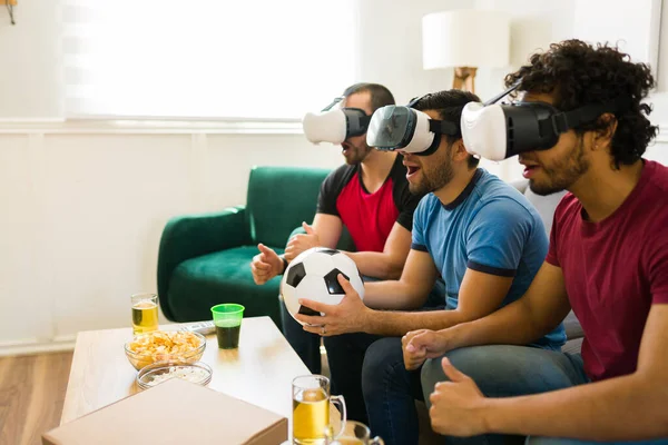Surprised male friends with VR glasses playing sports video games and having fun with virtual reality