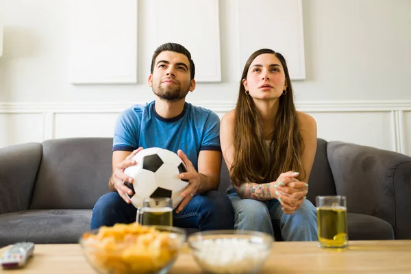 Beautiful young couple sitting on the sofa and enjoying a soccer game on TV
