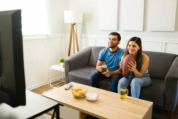体育迷一边看电视上的足球比赛一边笑着 一边喝啤酒和吃零食 — 图库照片