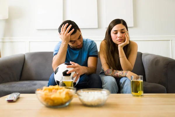Sad young woman and man and sports fans feeling disappointed after watching a soccer game on tv