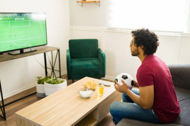 Latin spor taraftarı televizyonda şampiyonluk maçını izlerken elinde futbol topu tutuyor.