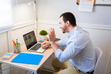 Mutlu Kafkasyalı adam evde çalışırken online bir toplantıya ya da video görüşmesine el sallıyor.