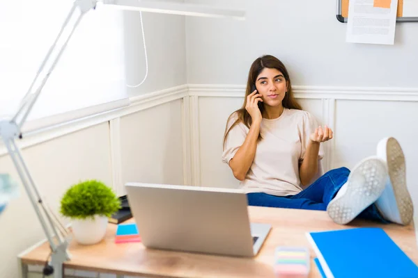 Busy casual young woman at home talking on the phone with a client while relaxing and working at her sunny office