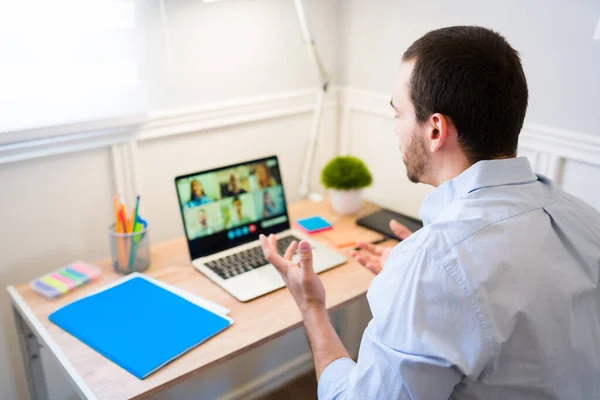 Young professional man seen from behind having a video call on the laptop at his work office