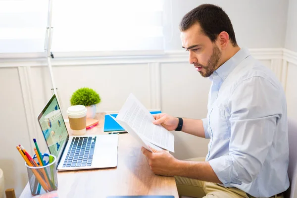 Ofis Masasında Dizüstü Bilgisayarla Otururken Kağıtlarını Satış Sözleşmelerini Okuyan Konsantre — Stok fotoğraf