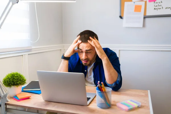 Stressed young man rubbing his head and feeling tired while sitting at his desk while working from home