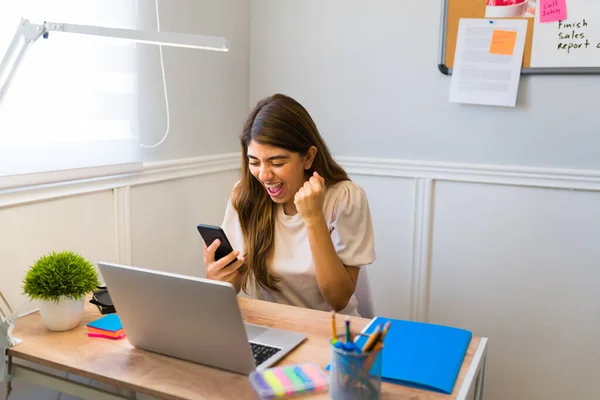 Successful woman shouting with happiness and celebrating while receiving good news on a text message while working from home