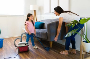 Happy beautiful young child vacuuming the living room and helping her mom with chores and clean the house 