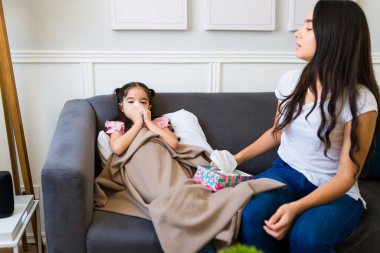 Hasta, üzgün küçük kız kameraya bakıyor ve endişeli annesiyle soğuk algınlığından kurtulurken burnunu siliyor. 