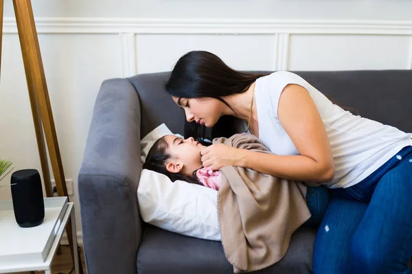 Loving Latin Mom Hugging Giving Kiss While Tucking Blanket Her — Zdjęcie stockowe
