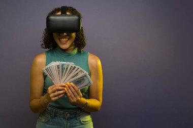 Cheerful woman in her 20s with virtual reality glasses earning a lot of money with virtual reality technology against a studio background