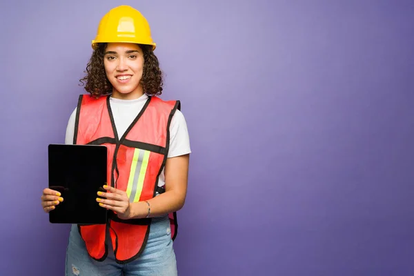 Happy female engineer smiling using a tablet while working on the construction field in front of a purple background with copy space