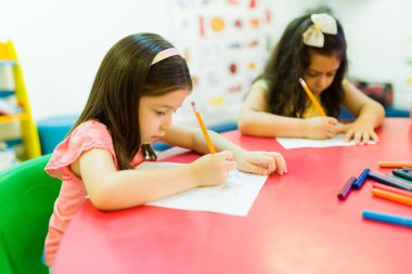 Diverse girls students writing and drawing together while doing class work during a preschool lesson 