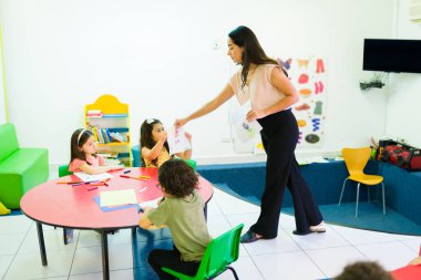 Anaokulu öğretmeni, anaokulu öğrencilerinin çizimlerine bakıyor. 