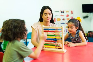 Çekici anaokulu öğretmeni abaküs kullanarak numaraları öğretiyor ve anaokulu öğrencilerine sayıyor.
