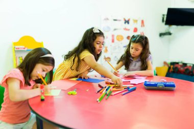 Anaokulu öğrencilerinin arkadaşlarıyla resim çizerken ve resim çizerken birlikte çalışan ve öğrenen çeşitli anaokulu öğrencileri.