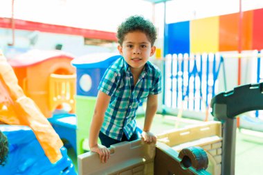 Cute latin elementary boy having fun and playing in the playground while learning in the kindergarten school