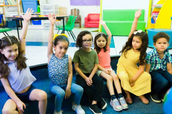 Diverse group of kindergarten boys and girls raising their hands to participate during a preschool lesson