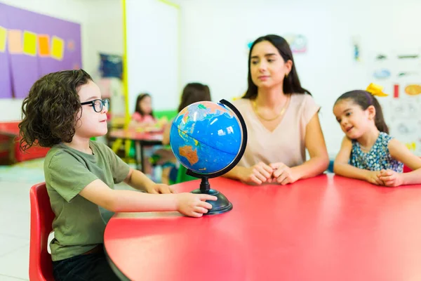 Smart young boy learning the world countries using a globe during a geography lesson with her kindergarten teacher