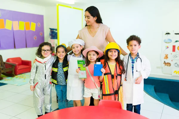 Happy preschool teacher hugging her kindergarten students while celebrating profession day dressed as astronaut, engineer, doctor and cheg at elementary school