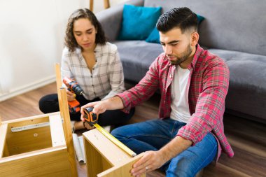 Yakışıklı genç adam, yeni mobilyaları bantla ölçüyor. Evde eşiyle birlikte bir masa kuruyor. 