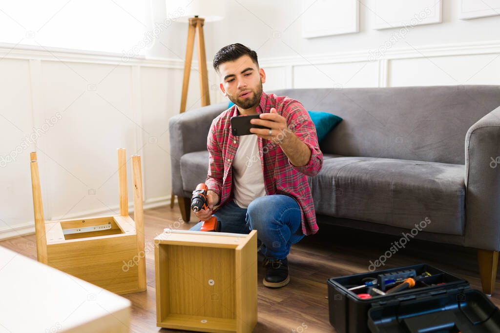 Handsome caucasian man watching a video tutorial on the smartphone to learn to do home improvements