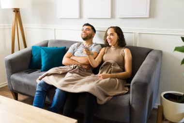 Neşeli genç çift oturma odasında birlikte gülüp eğlenirken uzaktan kumandayla televizyon seyrediyor.