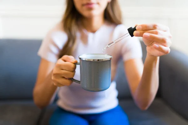 Focus on foreground of a mexican woman holding a pipette with medicine oil or vitamins supplement on her hot tea