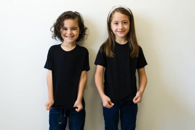 Cheerful boy and girl showing the front design print of their black mockup t-shirt against a white studio background