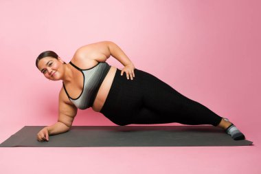 Cheerful hispanic overweight woman doing a side plank while exercising and having a fitness healthy lifestyle to lose weight
