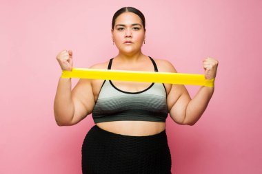 Active hispanic woman using a stretching band and working out with weight loss exercises for a healthy lifestyle 
